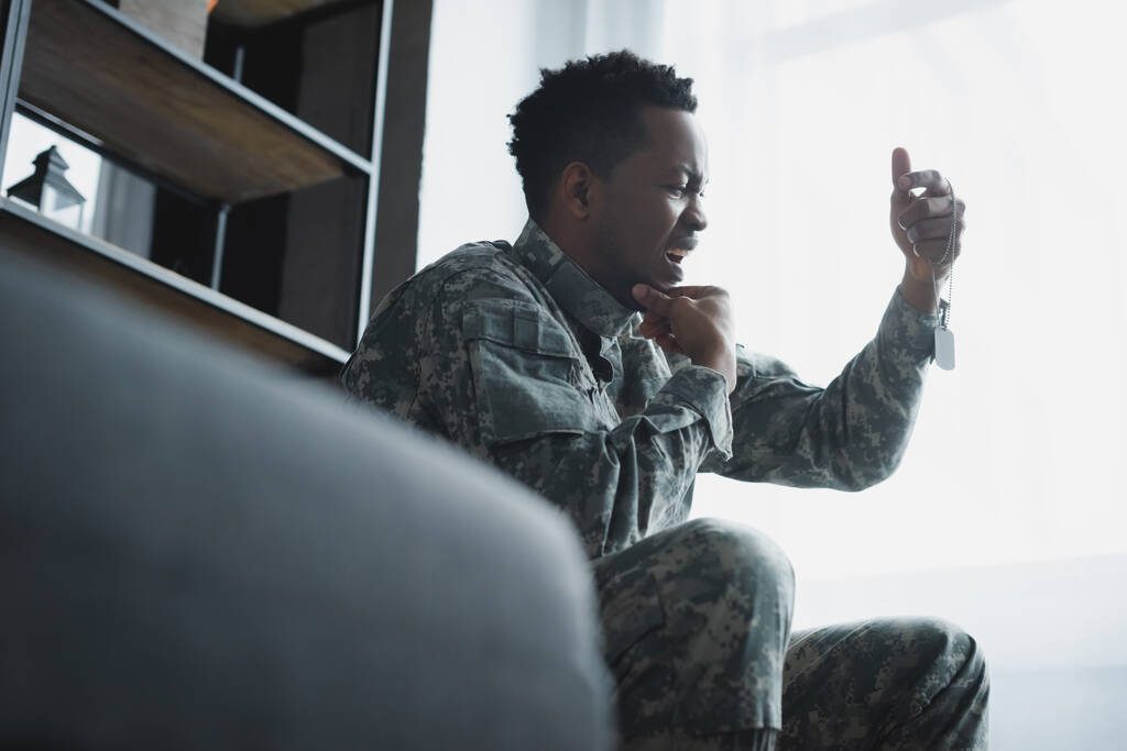 gestresster afrikanisch-amerikanischer Soldat weint und hält Armeeabzeichen zu Hause, leidet an PTBS - Foto, Bild