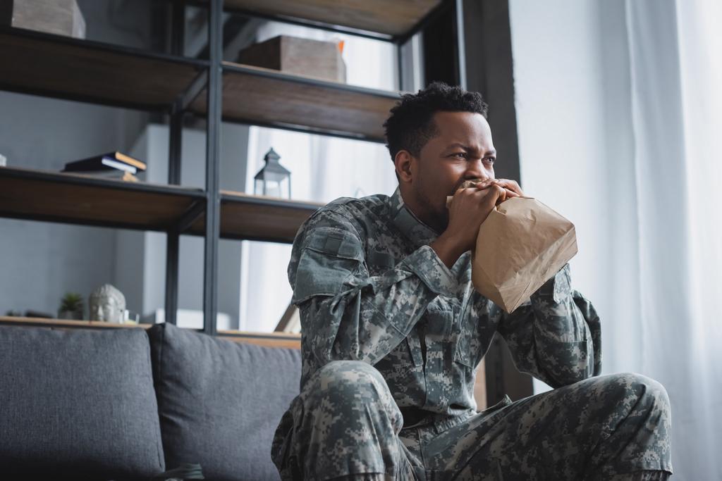 アフリカ系アメリカ人兵士が家庭でPTSDを患いパニック発作を起こしながら紙袋で呼吸するのを強調しました - 写真・画像