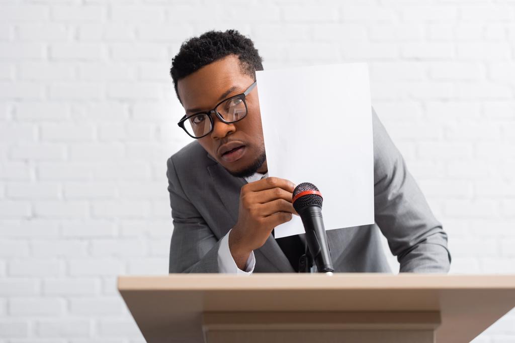 verängstigter afrikanisch-amerikanischer Redner versteckt sich während einer Konferenz hinter Papier - Foto, Bild