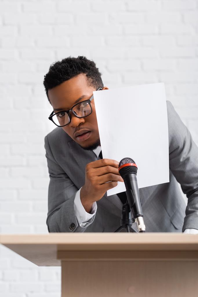 испуганный африканский американский оратор прячется за бумагой во время деловой конференции
 - Фото, изображение