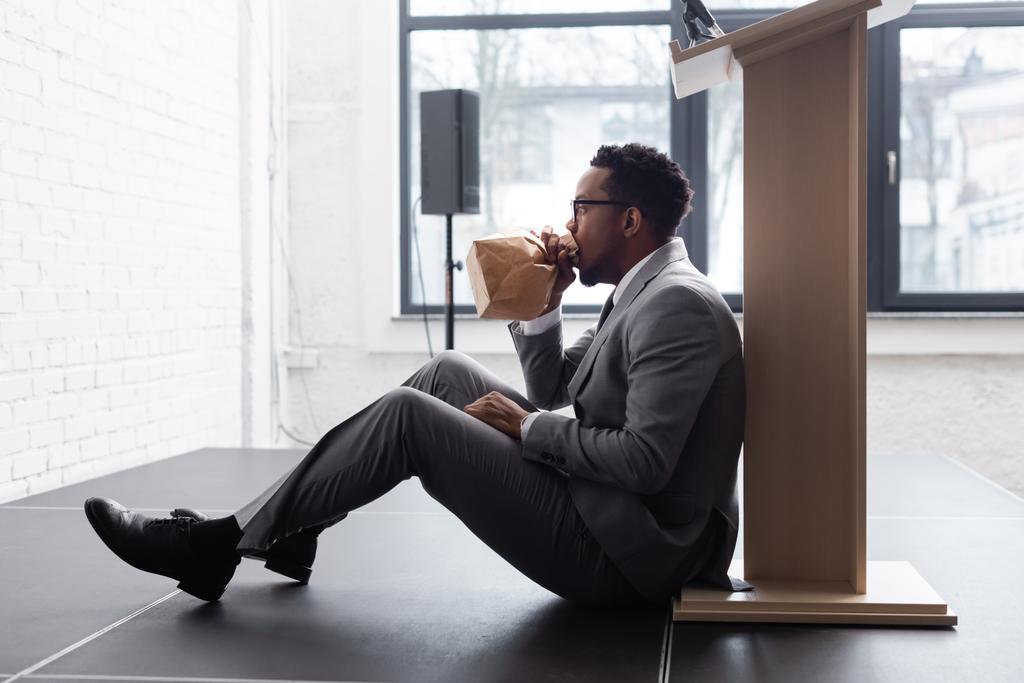 νευρικό αφροαμερικανός ομιλητής αναπνέει με χάρτινη σακούλα και έχει κρίση πανικού κατά τη διάρκεια επιχειρηματικού συνεδρίου στο γραφείο  - Φωτογραφία, εικόνα