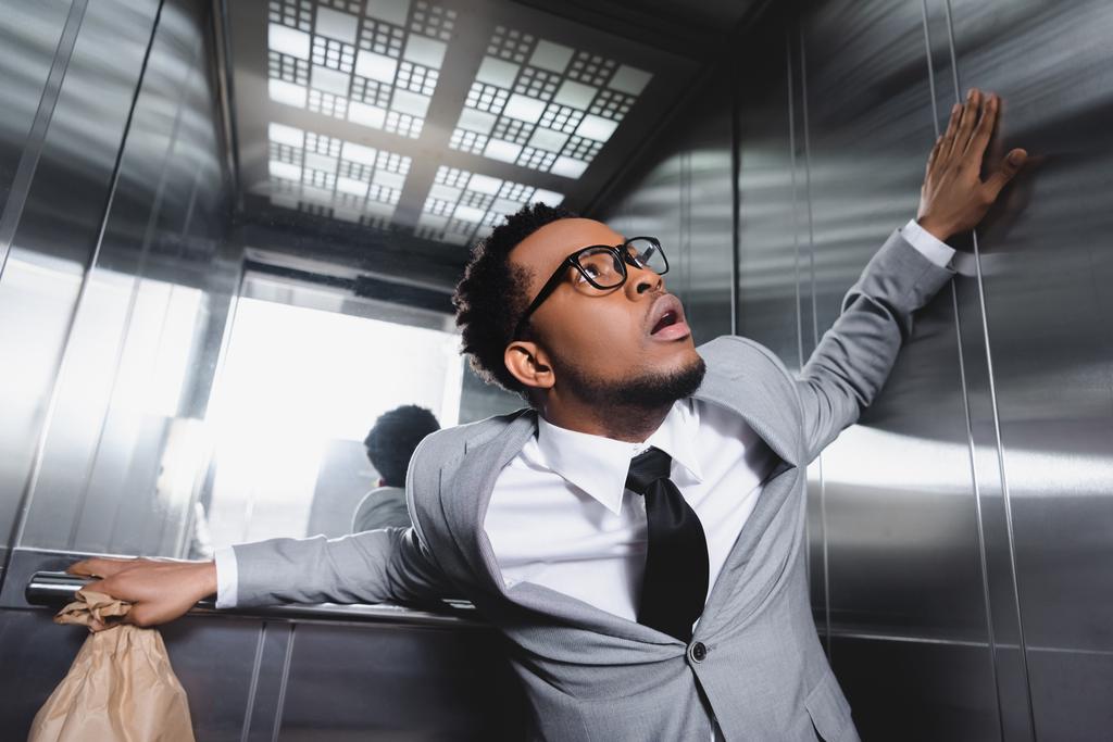 испуганный африканский американский бизнесмен с бумажным пакетом, страдающий от панической атаки в лифте
 - Фото, изображение