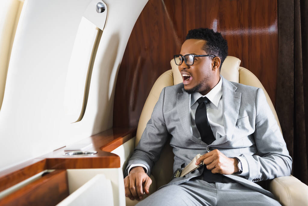 benadrukte Afro-Amerikaanse zakenman met veiligheidsgordel en een paniekaanval tijdens de vlucht op prive-vliegtuig - Foto, afbeelding
