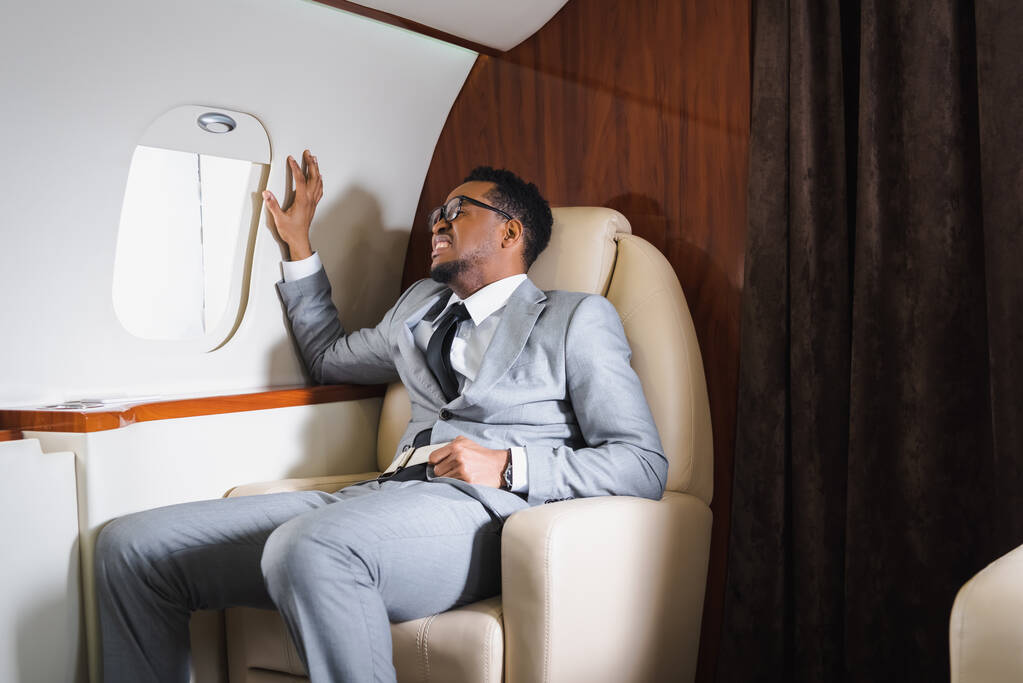 nervöser afrikanisch-amerikanischer Geschäftsmann mit Sicherheitsgurt und Panikattacke während Flug im Privatflugzeug - Foto, Bild