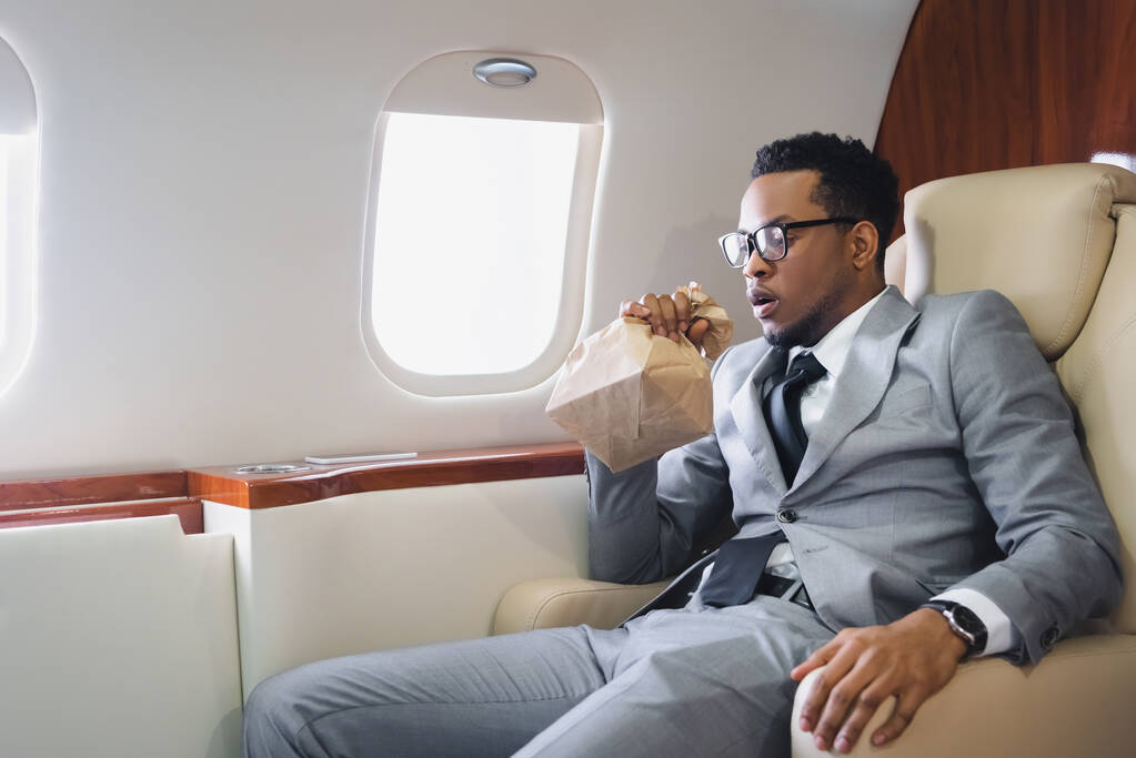 Homme d'affaires afro-américain inquiet respirant avec un sac en papier tout en ayant une attaque de panique pendant le vol en avion privé
 - Photo, image
