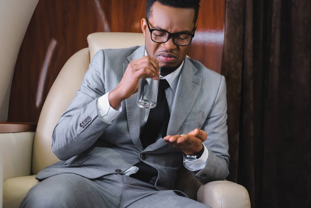 nervöser afrikanisch-amerikanischer Geschäftsmann nimmt Tabletten während er Übelkeit oder Panikattacke während des Fluges im Privatflugzeug hat - Foto, Bild