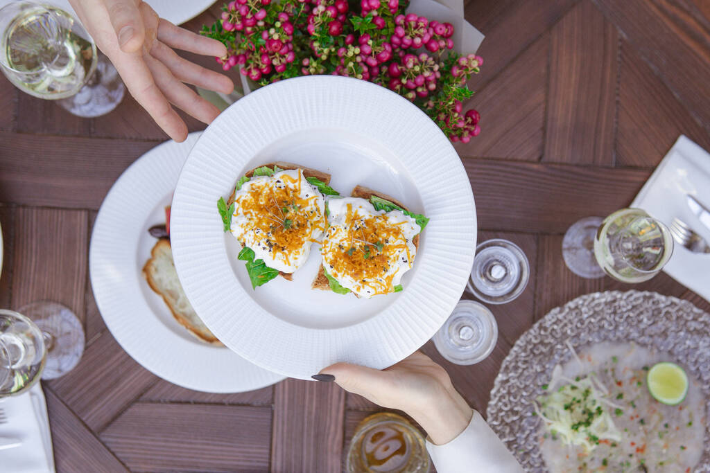 вид сверху женских рук, держащих тарелку со свежими овощами и сыром на столе
 - Фото, изображение