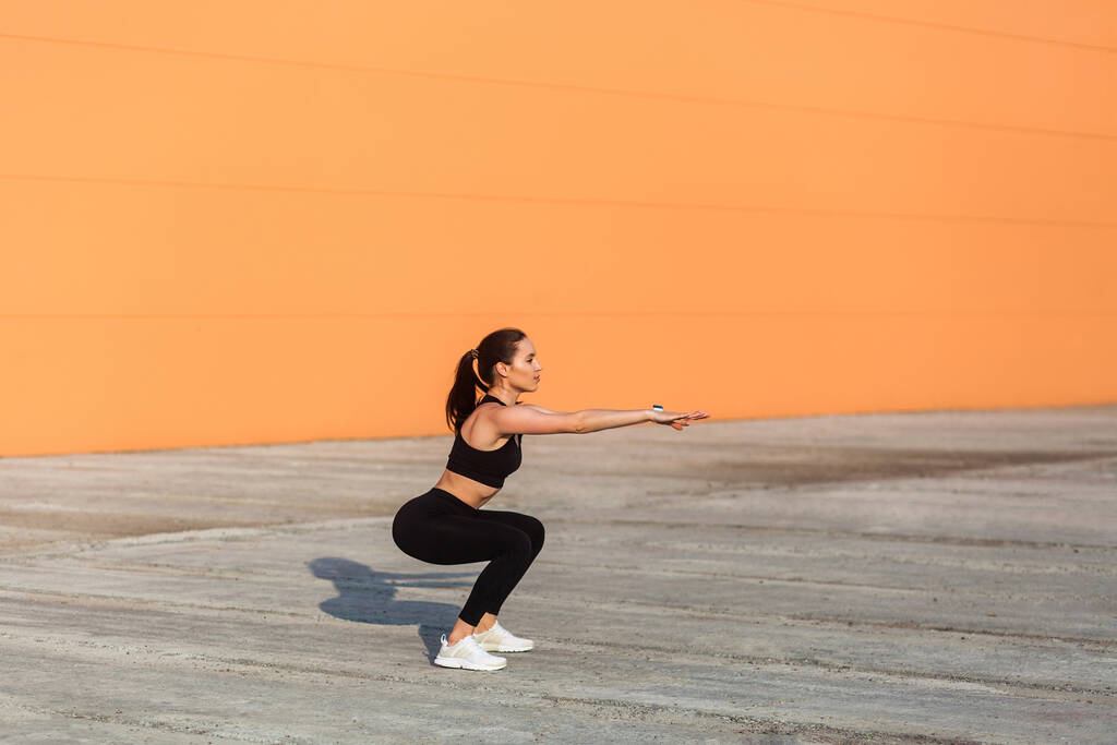 Fit νεαρή γυναίκα σε σφιχτό αθλητικό ντύσιμο, μαύρο παντελόνι και κορυφή, εξάσκηση σε εξωτερικούς χώρους, κάνει split ή lunge κατάληψη άσκηση με τεντωμένα χέρια, χαμηλότερη σωματική άσκηση. Υγειονομική περίθαλψη, αθλητική δραστηριότητα - Φωτογραφία, εικόνα