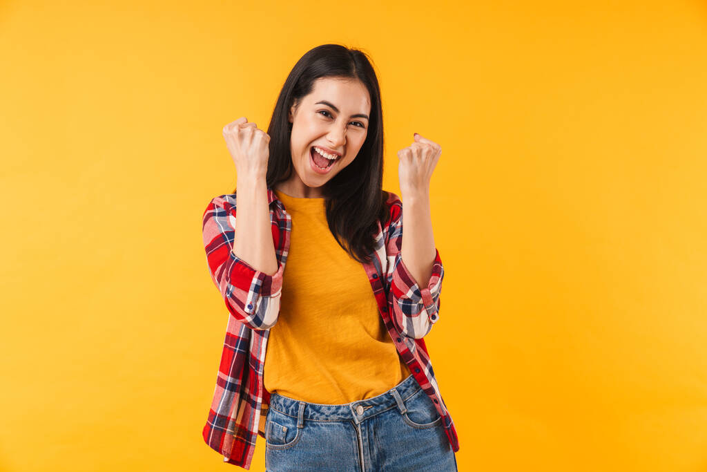 Fotografie vzrušené mladé ženy usmívat a dělat vítěz gesto izolované přes žluté pozadí - Fotografie, Obrázek