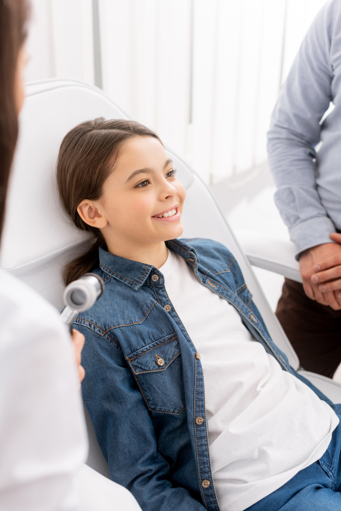 enfoque selectivo del niño sonriente cerca del padre y ent médico con otoscopio
 - Foto, imagen