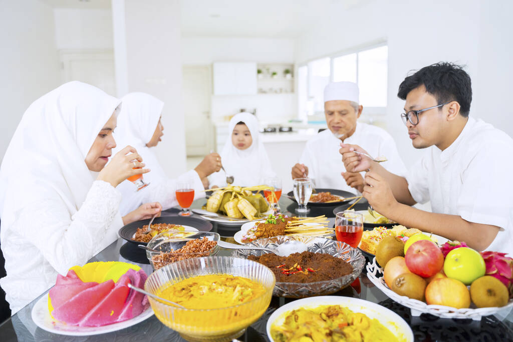 Portrait of Asian muslim family eating & drinking together while celebrating Idul Fitri in their dining room - Photo, Image