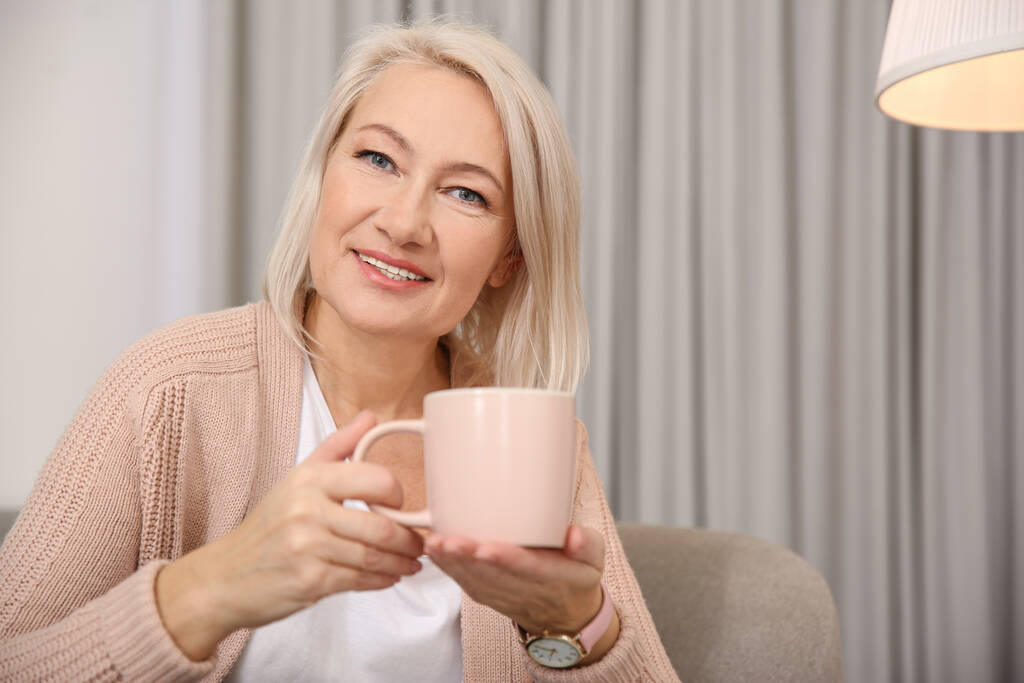 Beautiful mature woman with cup of coffee at home. Space for text - Photo, Image