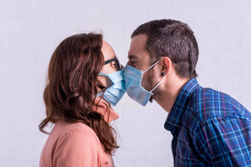 Mężczyzna i kobieta całują się w maskach medycznych, chronią przed wirusem. Pandemia. Koronawirus. - Zdjęcie, obraz