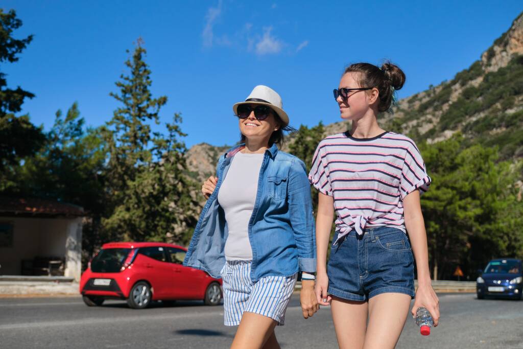 Twee vrouwen moeder en dochter tiener wandelen op zonnige zomerdag op bergweg. Toerisme, excursies, reizen, familievakanties - Foto, afbeelding