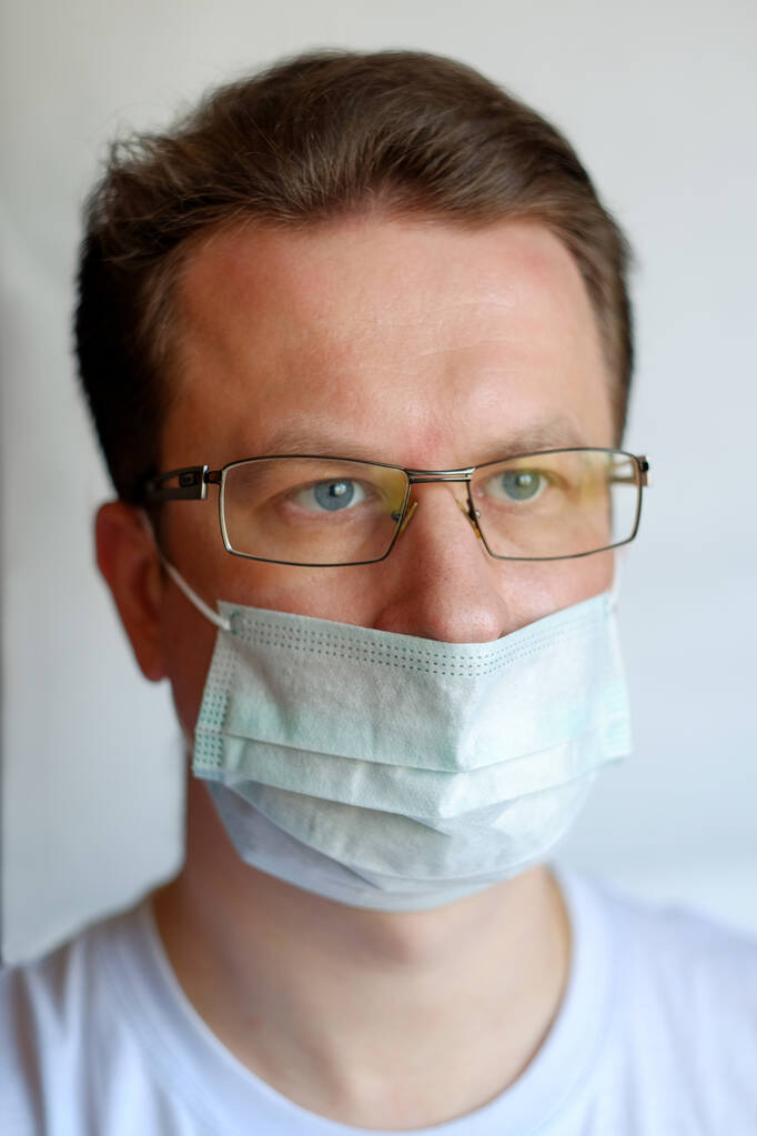 Ritratto ravvicinato di giovane uomo che indossa una maschera influenzale medica in piedi isolato su sfondo bianco. Macro colpo di uomo in maschera medica sul viso paura di epidemia COVID-19
 - Foto, immagini