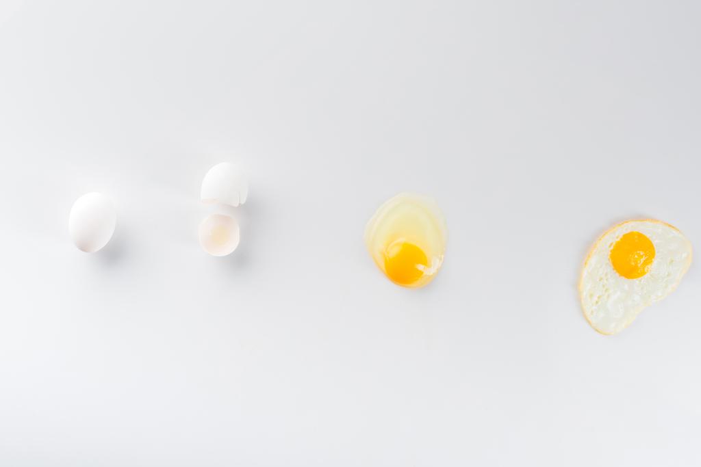 κορυφαία άποψη της μετατροπής των αυγών από ωμά σε τηγανητά σε λευκό  - Φωτογραφία, εικόνα