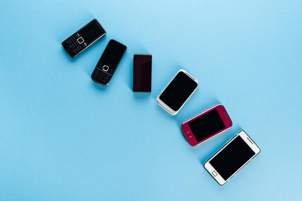 青と進化の概念におけるヴィンテージ携帯電話と現代のスマートフォンのトップビュー  - 写真・画像
