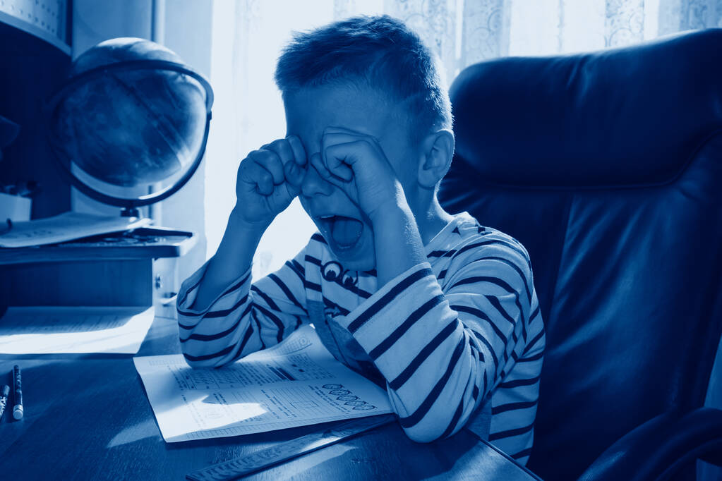 Ödev yaparken ağlayan ve çığlık atan okul çağındaki bir çocuk. 2020 yılının klasik mavi renginde ağır baskı eğitimi kavramı - Fotoğraf, Görsel