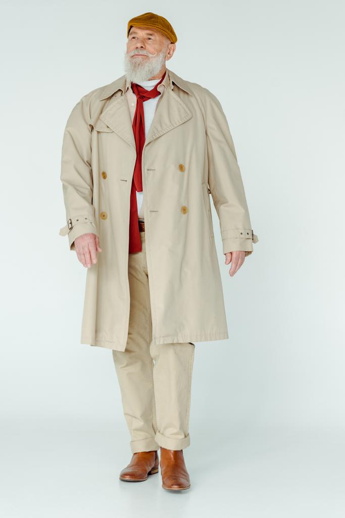 Volledige lengte van stijlvolle senior man in trench jas weg te kijken op witte achtergrond - Foto, afbeelding