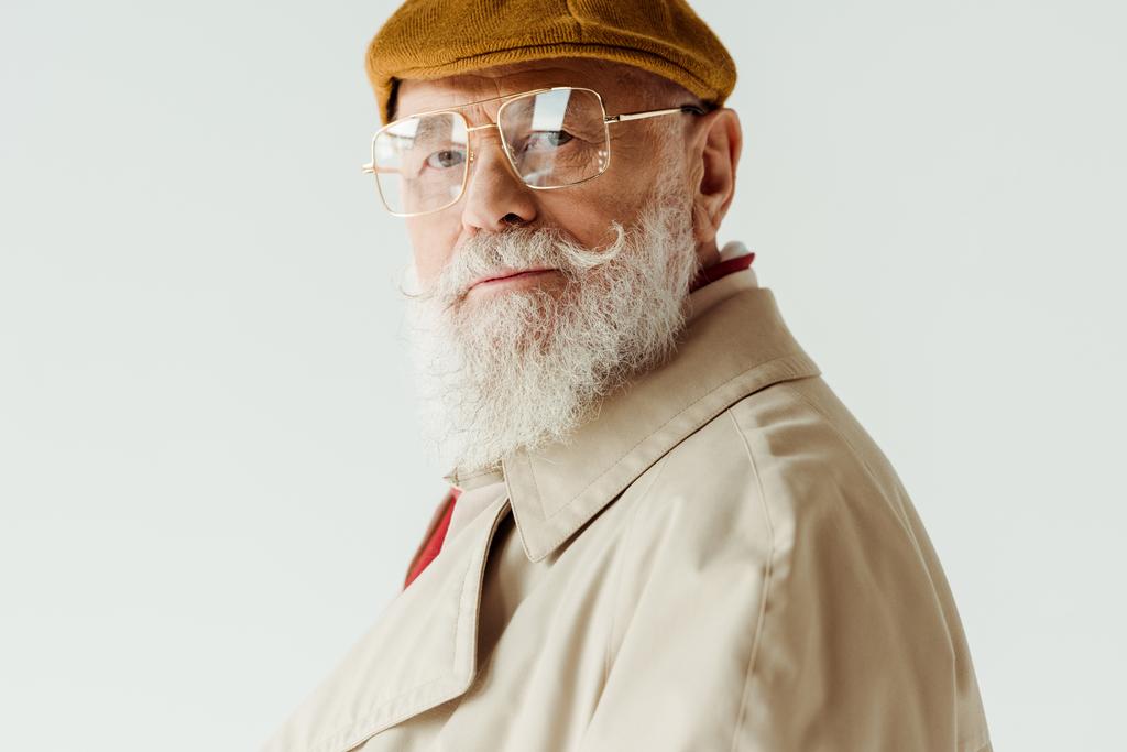 Seitenansicht eines modischen älteren Mannes mit Sonnenbrille und Mantel, der isoliert auf weiß in die Kamera blickt - Foto, Bild