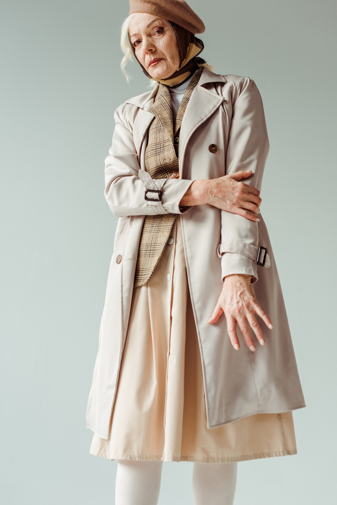 Mulher sênior em boina e casaco de trincheira olhando para câmera isolada em cinza
 - Foto, Imagem