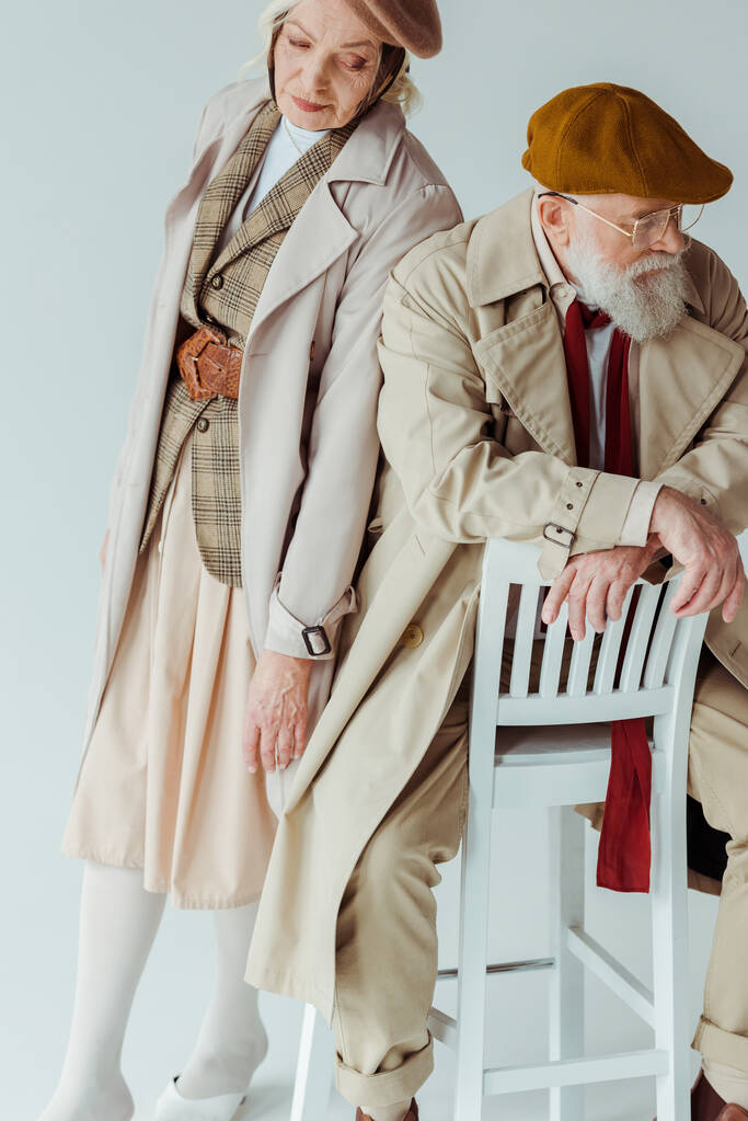 Елегантна старша жінка стоїть біля красивого чоловіка на стільці на білому тлі
 - Фото, зображення