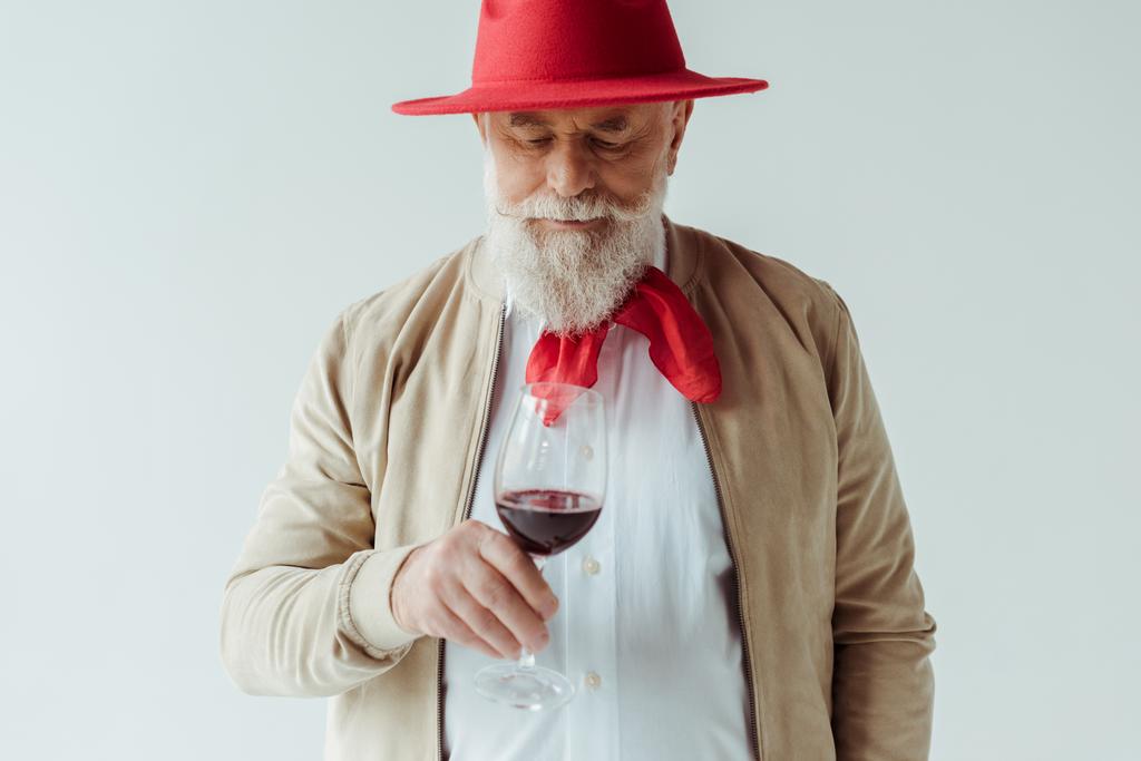 Beyaz şarap bardağını tutan kırmızı şapkalı yakışıklı yaşlı adam. - Fotoğraf, Görsel