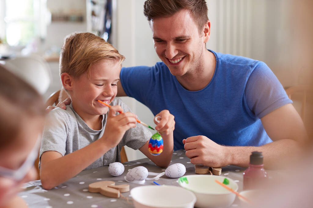 Padre con bambini seduti a tavola a decorare le uova per Pasqua a casa - Foto, immagini
