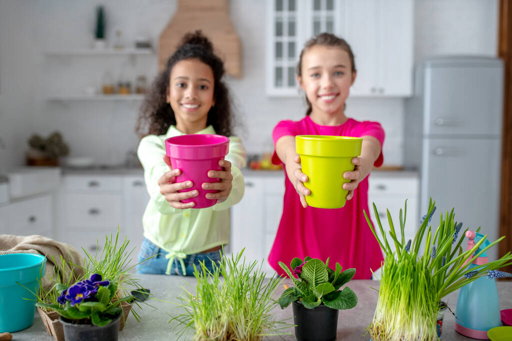 Twee schattige tieners tonen potten met bloemen - Foto, afbeelding