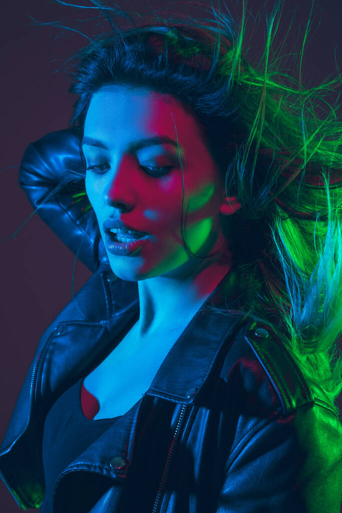 Mooie vrouwen portret met blazen haar op donkere studio achtergrond in kleurrijke neon licht - Foto, afbeelding
