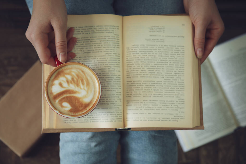 Vrouw met kopje koffie leesboek binnen, bovenaanzicht - Foto, afbeelding