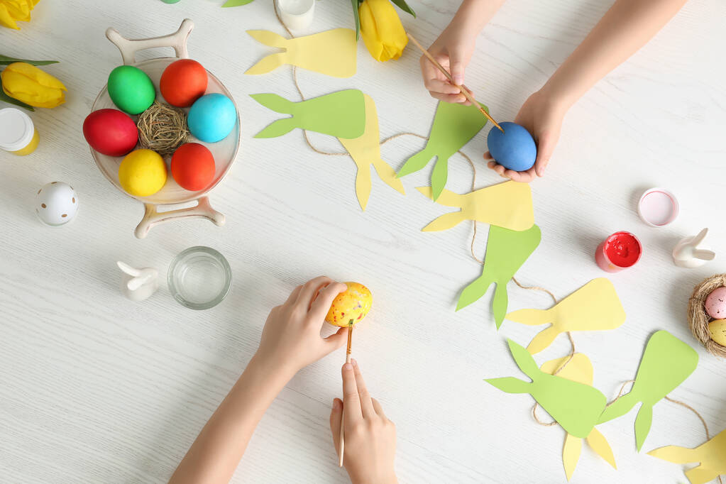 Küçük çocuklar Paskalya yumurtalarını beyaz ahşap masaya boyuyor. - Fotoğraf, Görsel