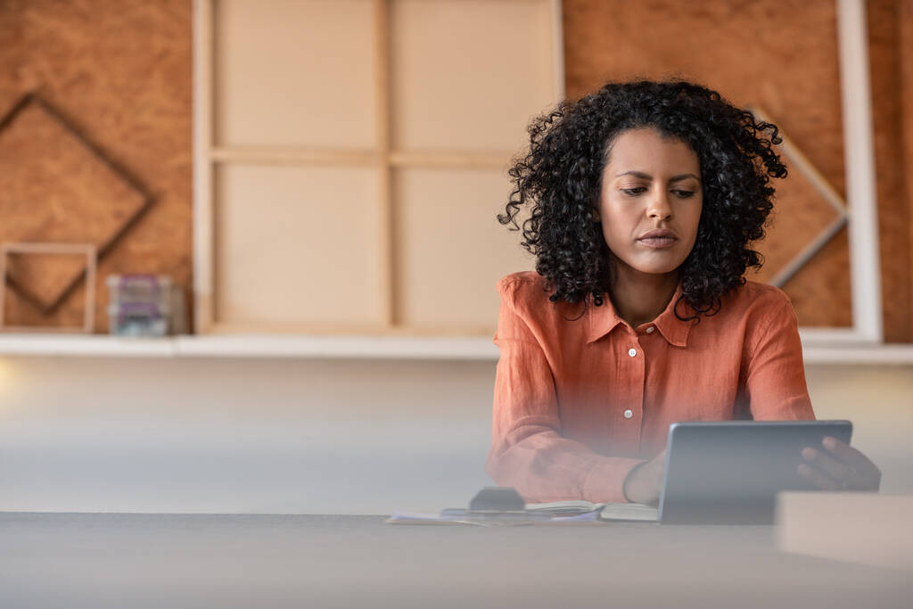 Junge Frau arbeitet online mit einem digitalen Tablet, während sie an einer Werkbank in ihrem Bilderrahmenstudio sitzt - Foto, Bild