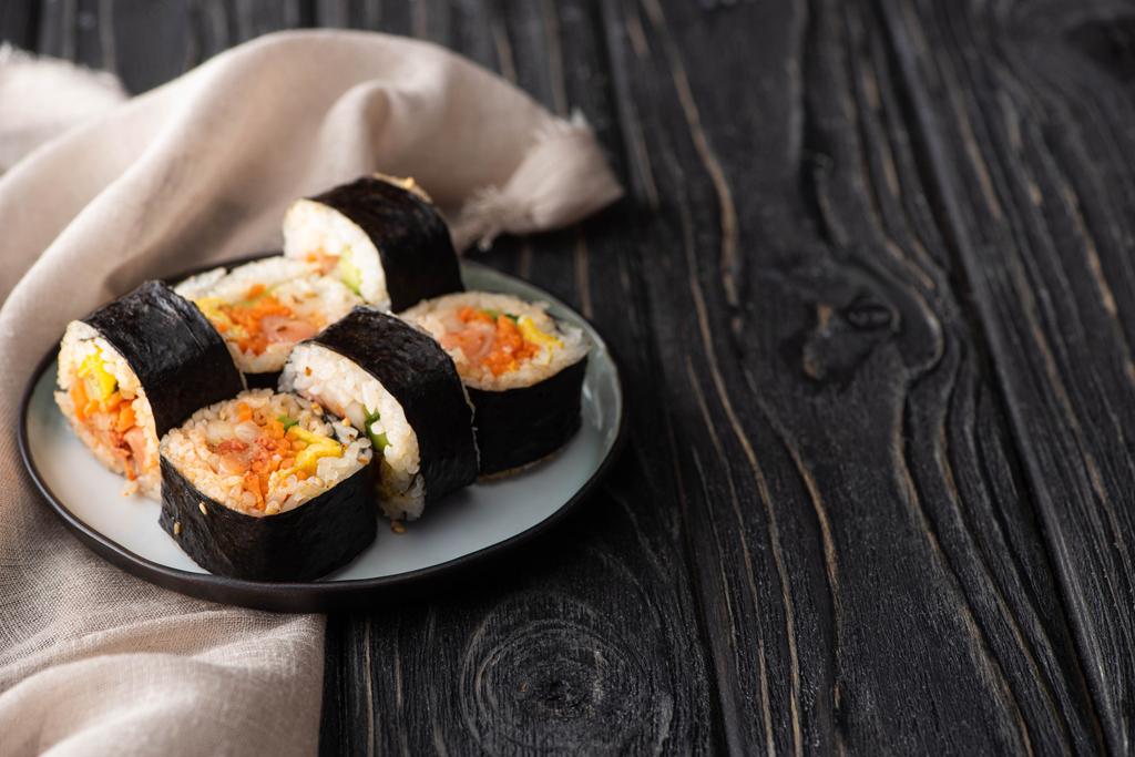 selective focus of tasty rice rolls with vegetables and salmon near cotton napkin on wooden surface  - Photo, Image