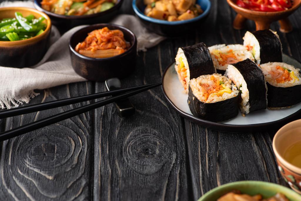 selective focus of delicious gimbap near korean side dishes and cotton napkin on wooden surface  - Photo, Image