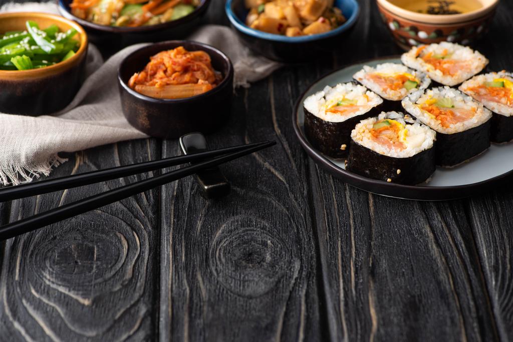 foyer sélectif de rouleaux de riz coréen près des plats d'accompagnement, baguettes et serviette de coton sur la surface en bois
  - Photo, image
