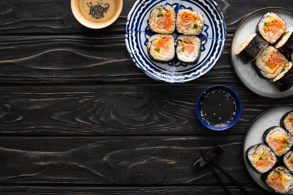 top view of sesame oil near plates with gimbap near chopsticks on wooden surface  - Photo, Image