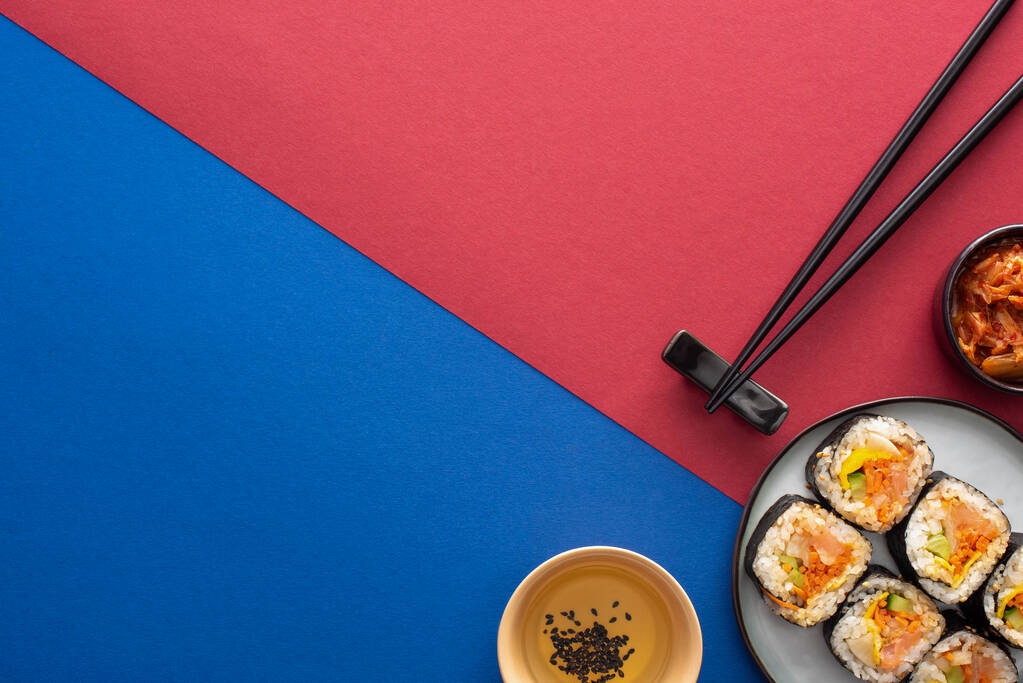 bovenaanzicht van plaat met heerlijke gimbap bij sesamolie en kimchi op karmozijn en blauw  - Foto, afbeelding