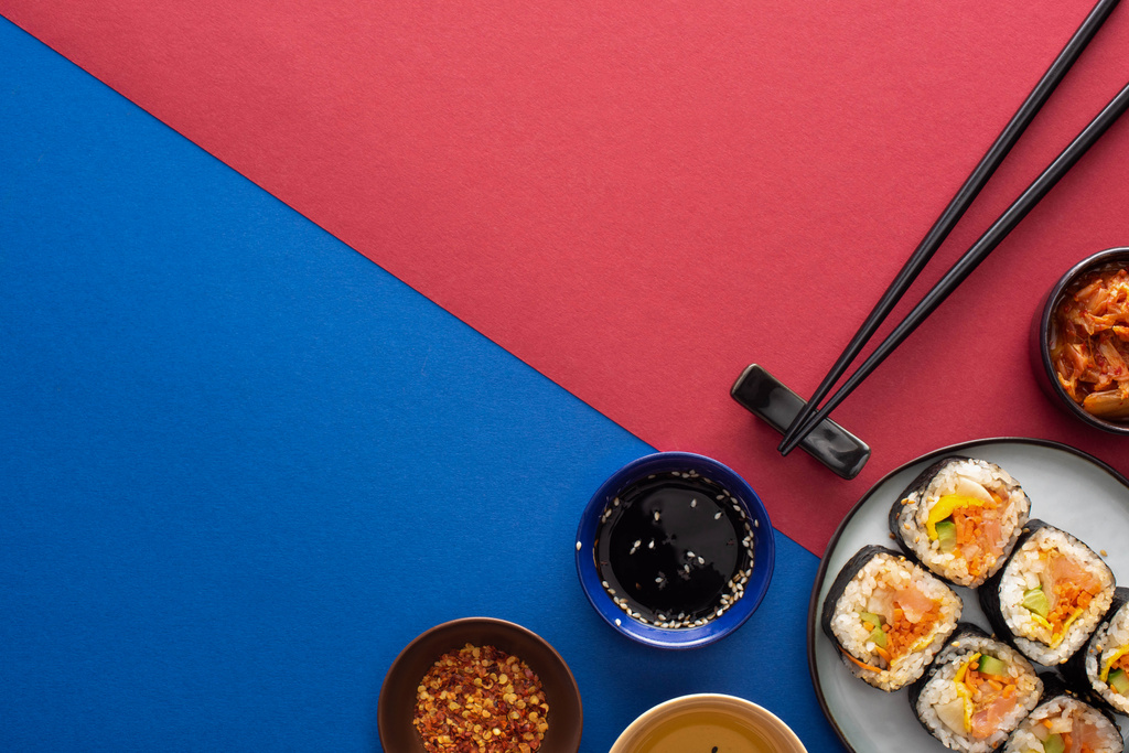 vista superior de la salsa de soja y aceite de sésamo cerca de gimbap en carmesí y azul
  - Foto, imagen