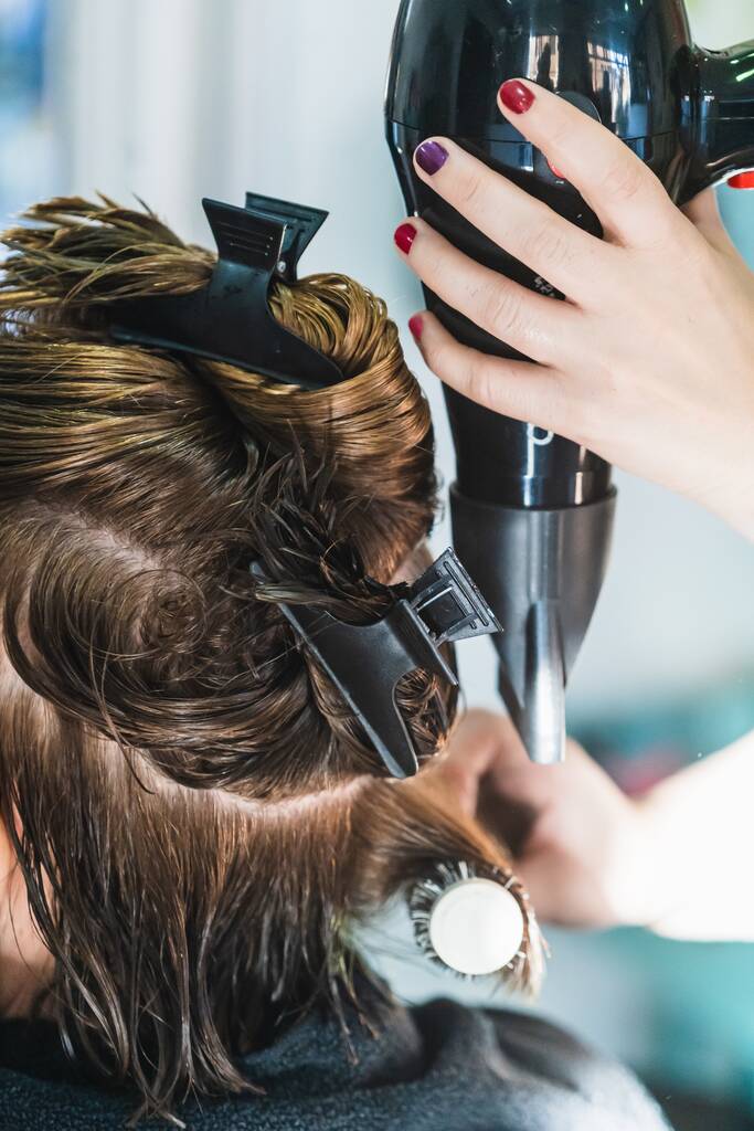 Вертикальний крупним планом знімок перукаря, який сушить коротке волосся жінки в салоні краси
 - Фото, зображення