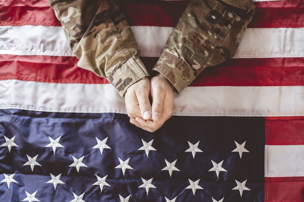 Ein amerikanischer Soldat trauert und betet mit der amerikanischen Flagge vor sich - Foto, Bild