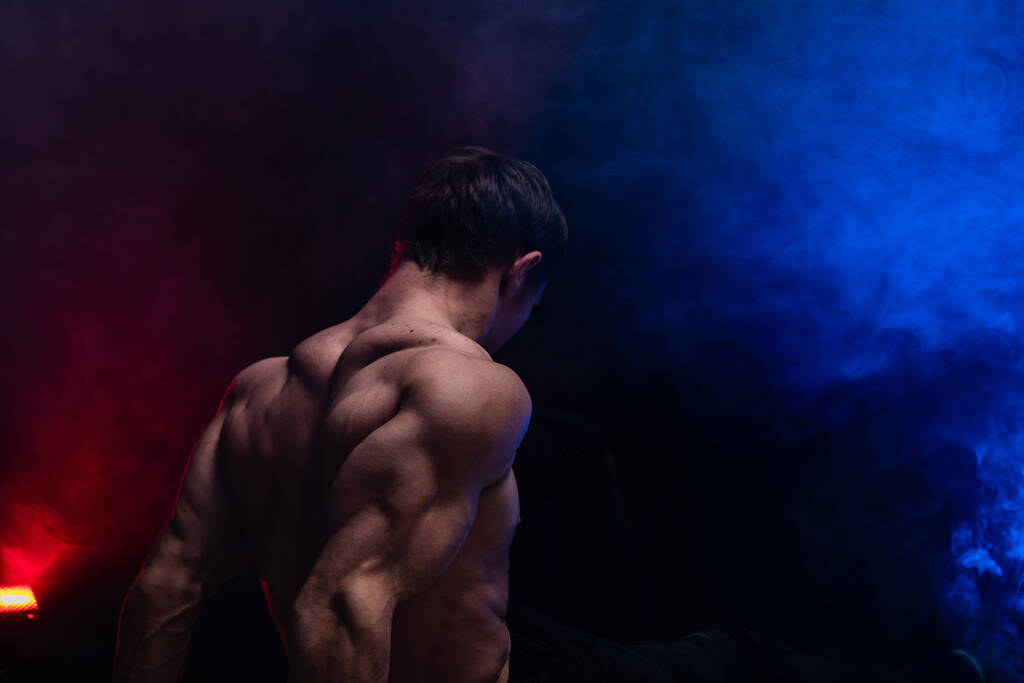 Muskularny mężczyzna pokazuje mięśnie odizolowane na czarnym tle z kolorowym dymem. Pojęcie zdrowego stylu życia  - Zdjęcie, obraz