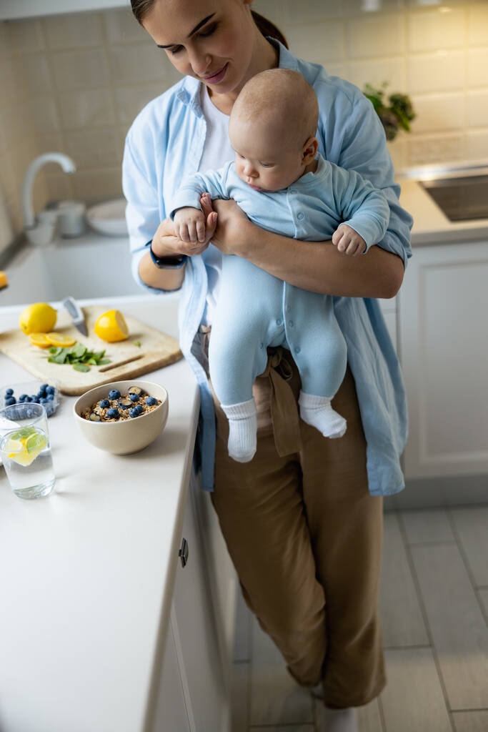 Улыбающаяся мать, стоящая со своим ребенком на кухне
 - Фото, изображение