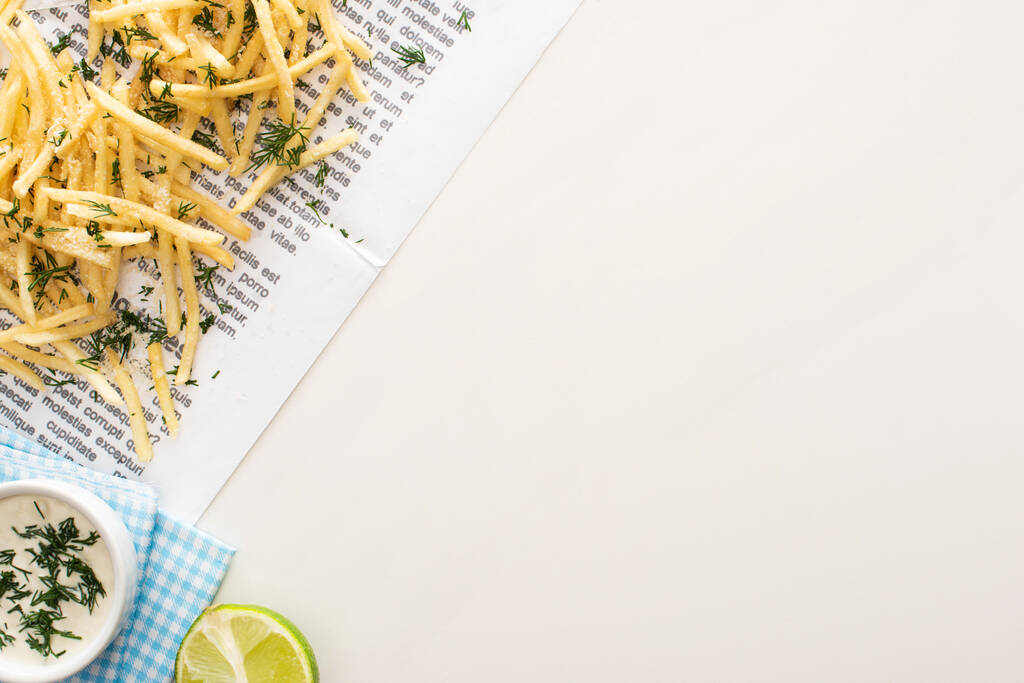 bovenaanzicht van frietjes, knoflooksaus en in plakjes gesneden limoen op krant op wit  - Foto, afbeelding
