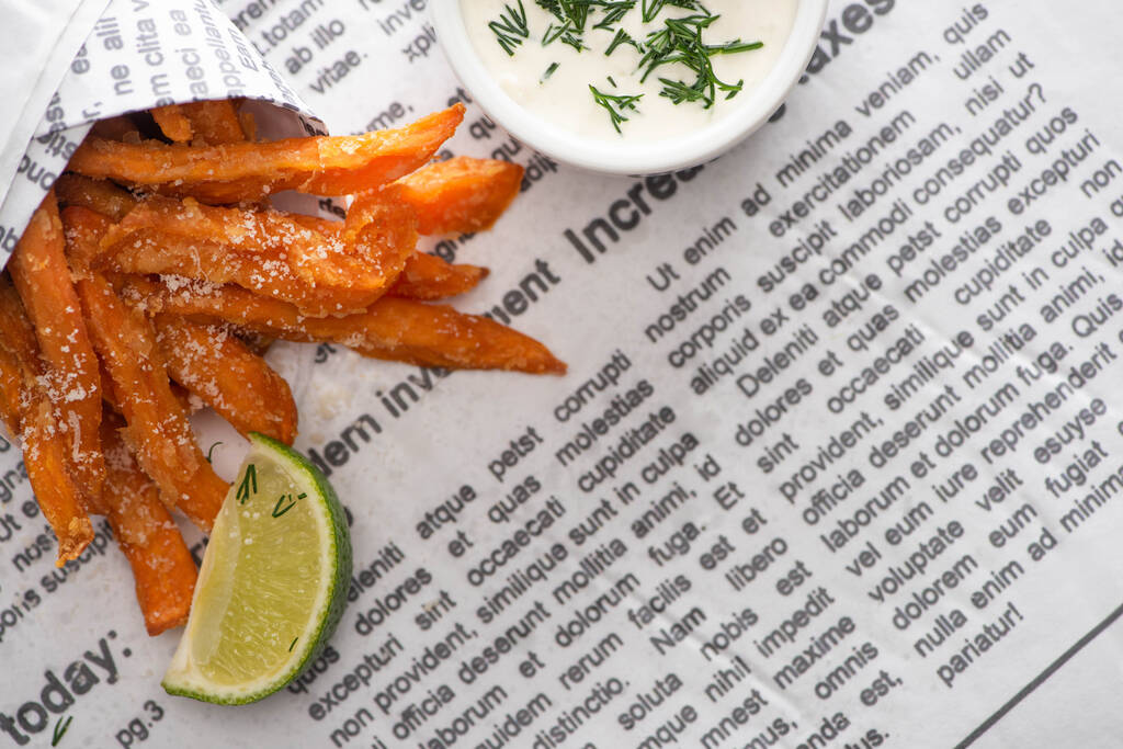 top view of crispy french fries, sliced lime and garlic sauce with dill on newspaper  - Photo, Image
