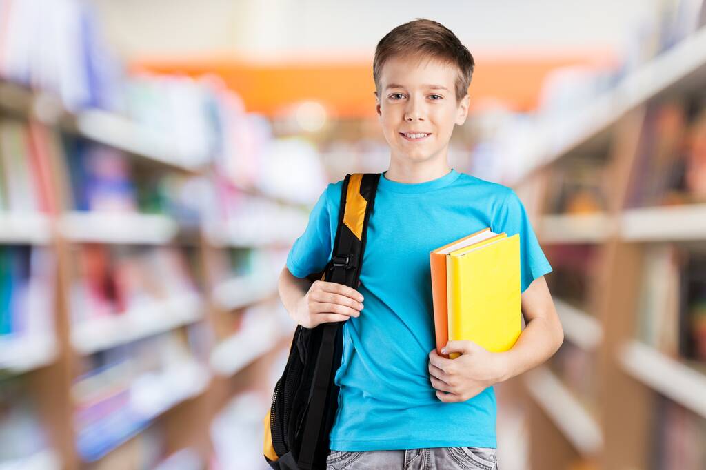 portrait of a cute schoolboy with books in library - Photo, Image