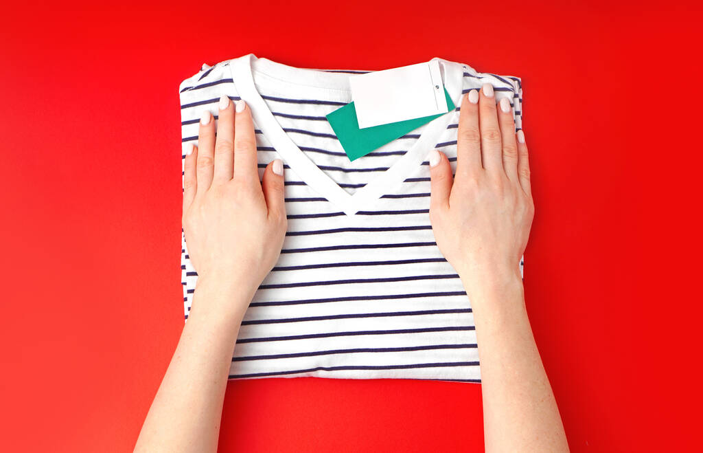 Vrouw vouwt nieuw t-shirt op een rode achtergrond. Bovenaanzicht. Kopieerruimte.  - Foto, afbeelding