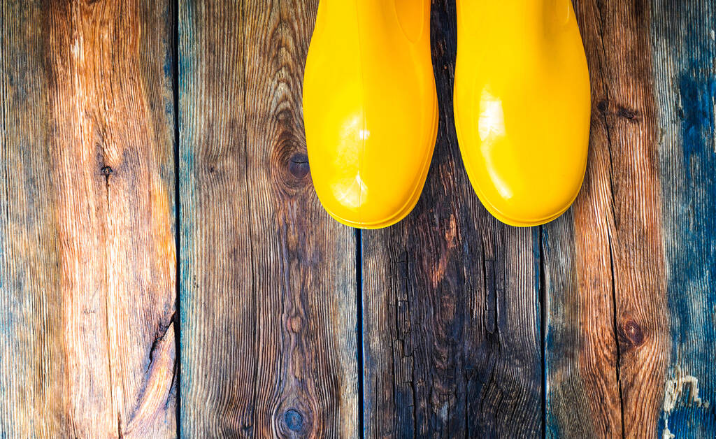 Botas de lluvia amarillas en una terraza climatizada de madera húmeda
 - Foto, imagen