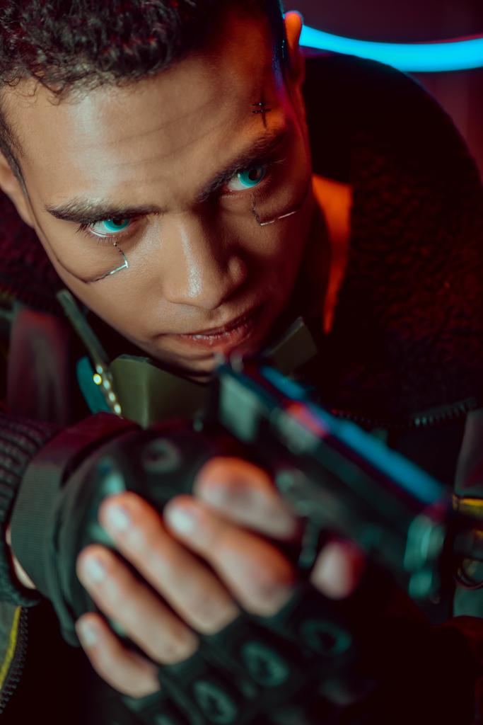 επιλεκτική εστίαση των ένοπλων bi-φυλετικών cyberpunk player με μεταλλικές πλάκες στο πρόσωπο κρατώντας όπλο  - Φωτογραφία, εικόνα
