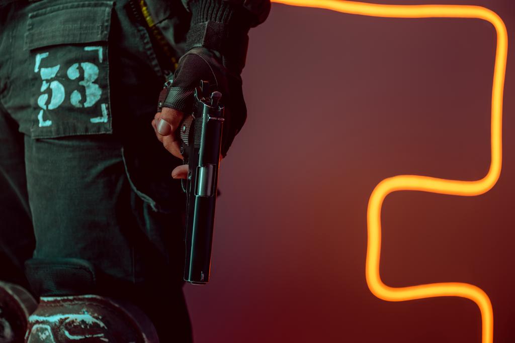 vista recortada de jugador cyberpunk peligroso con pistola en negro con iluminación de neón
  - Foto, imagen